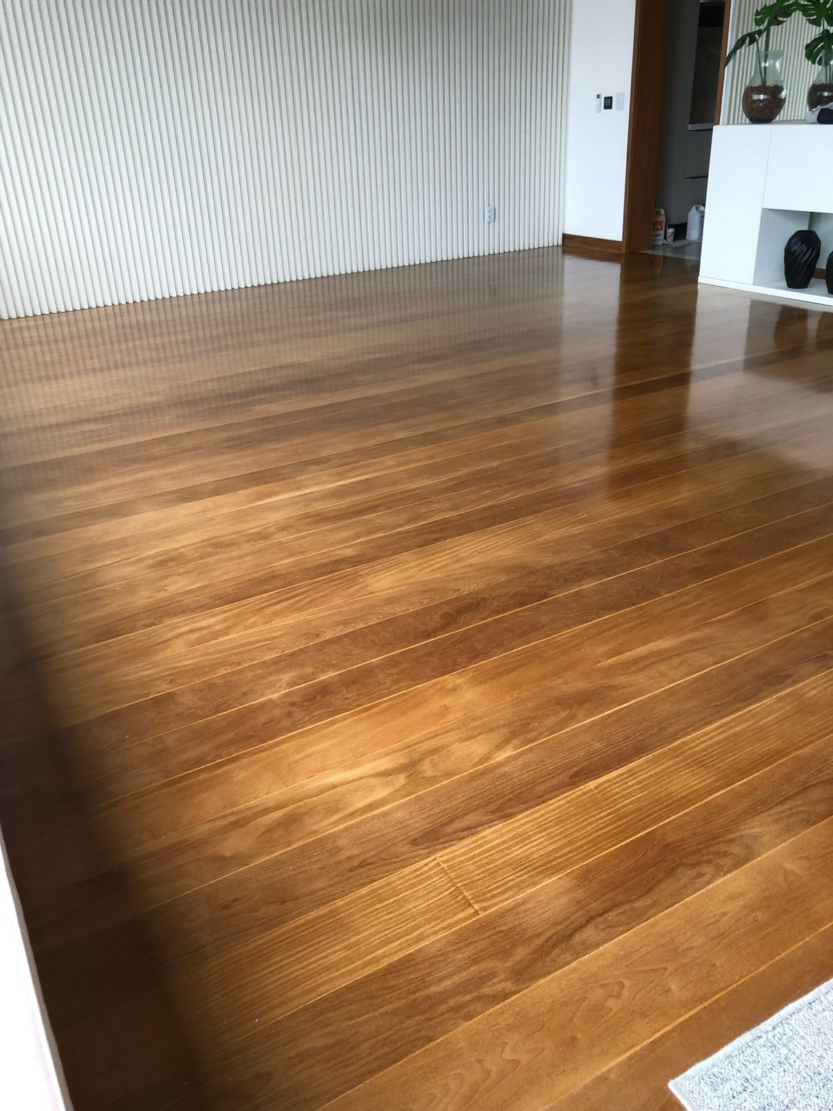 Sala ampla com piso de madeira cor de mel e acabamento brilhante